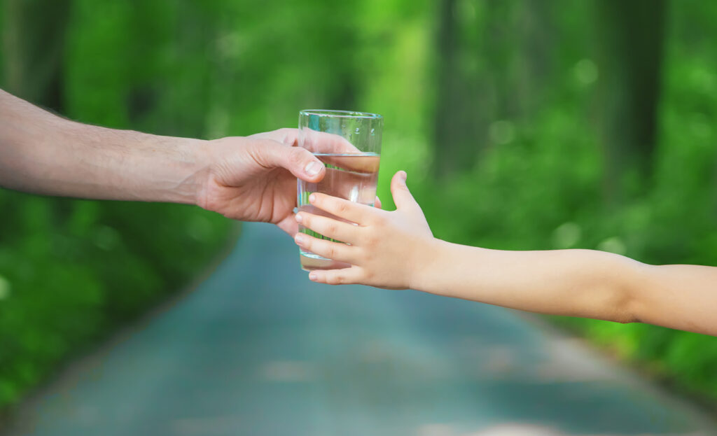 Ojciec podaje dziecku szklankę świeżej wody. Selektywna ostrość. Natura.